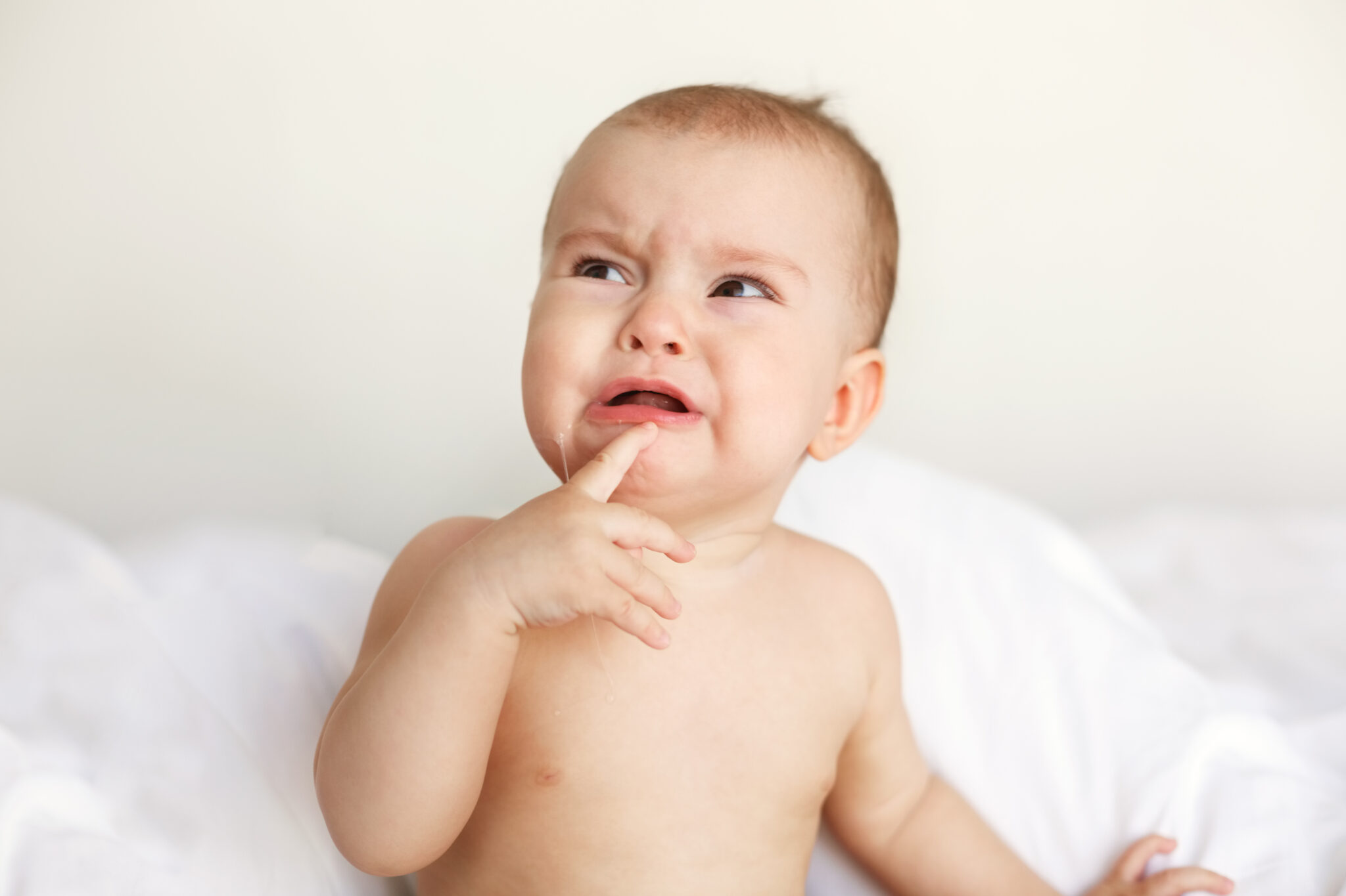 Cute nice little baby girl crying lying with her mom on bed at home.