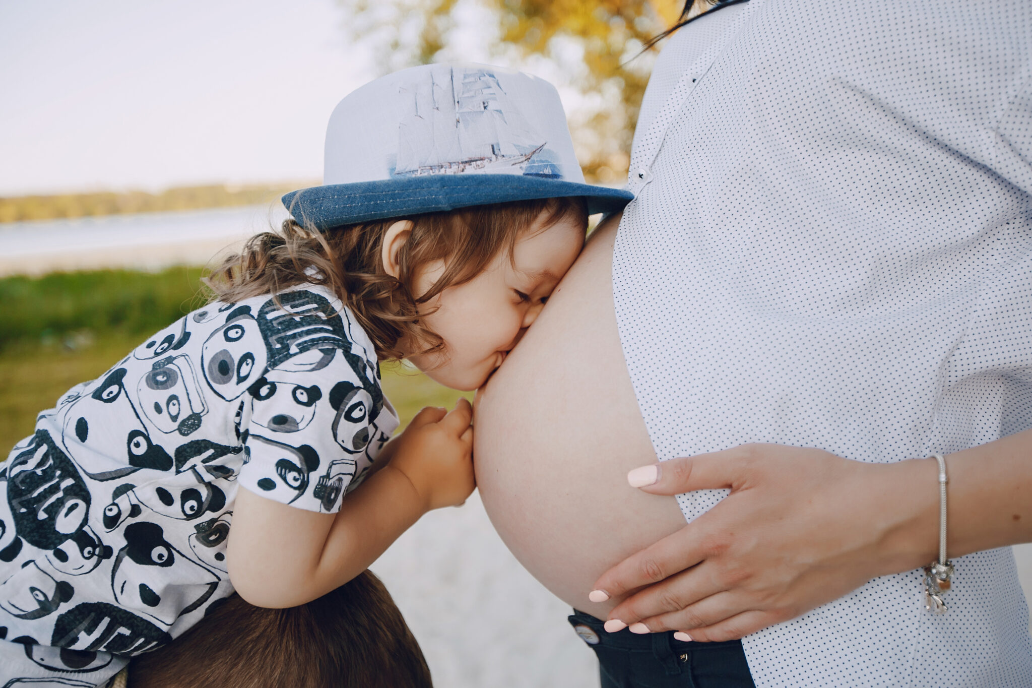 Young and beautiful pregnant brunette in a white shirt on a beach with her little son