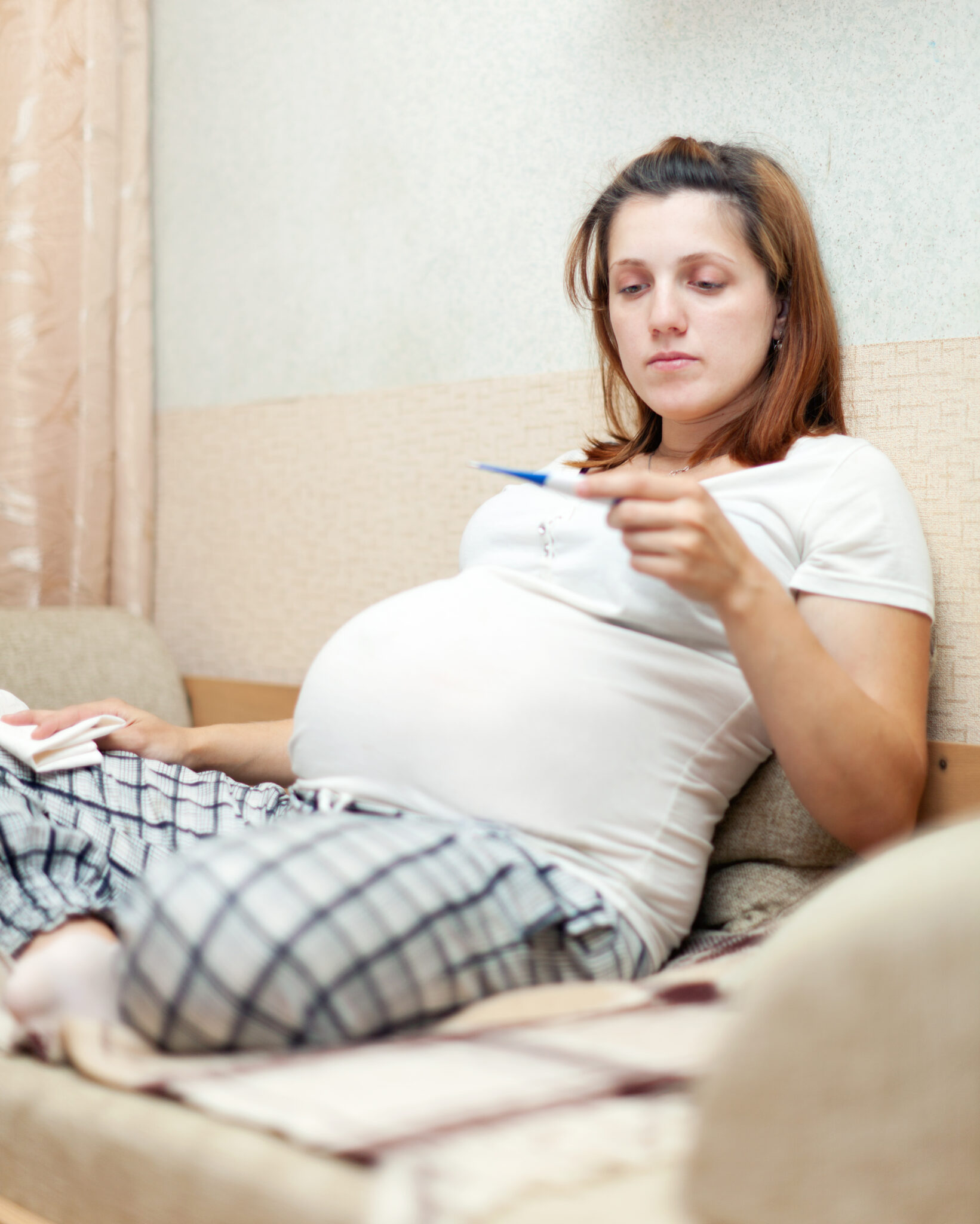 pregnant woman holding thermometer in home