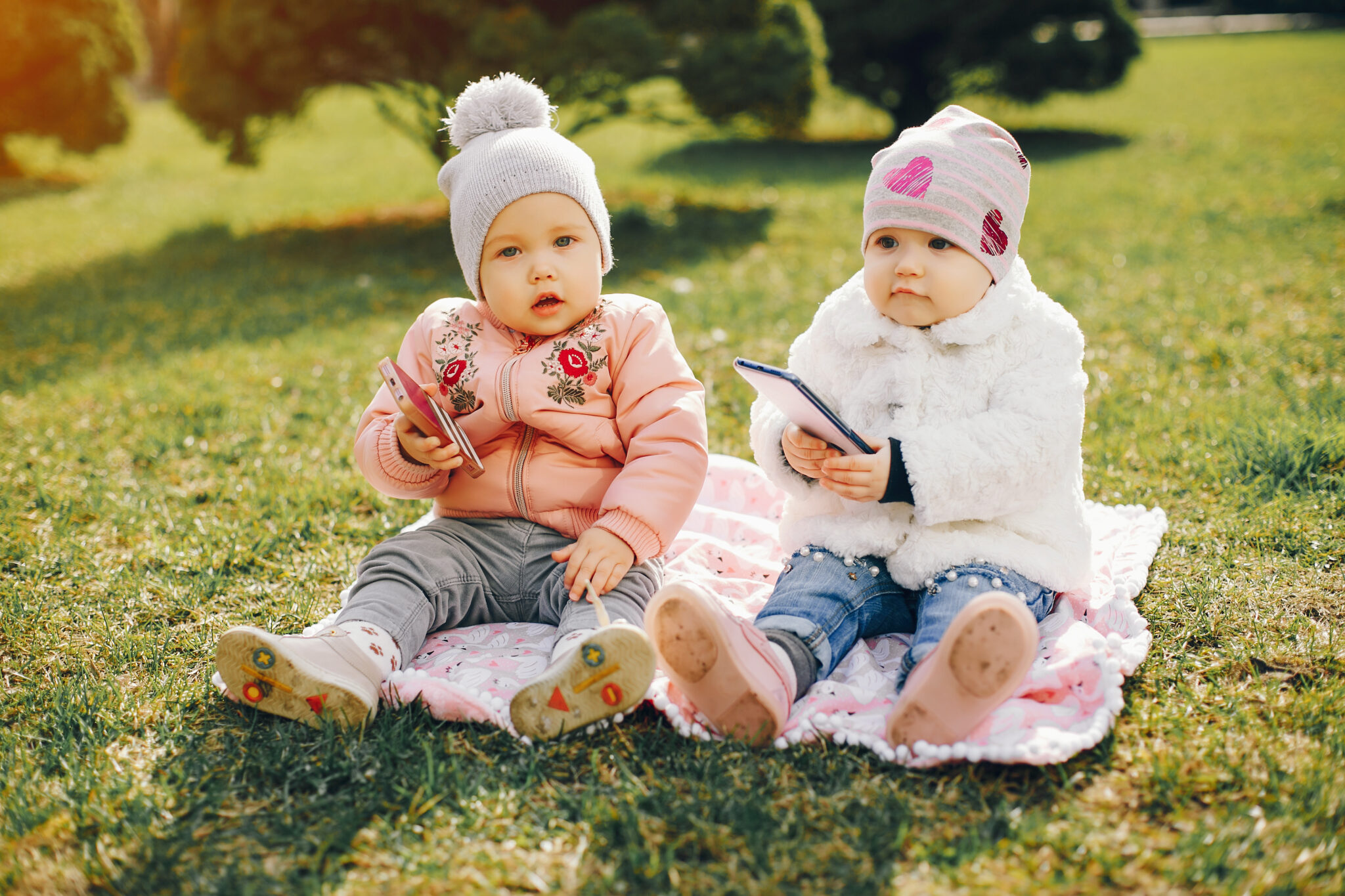 little girl in a white coat and in a hat with her little sister in a pink jacket sitting