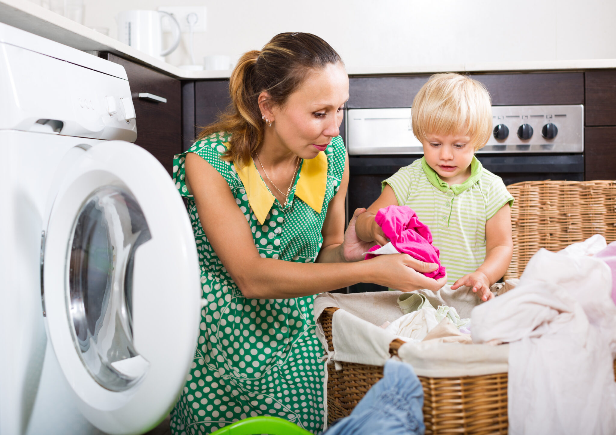 Family laundry. Happy woman with child putting clothes in to washing machine at home