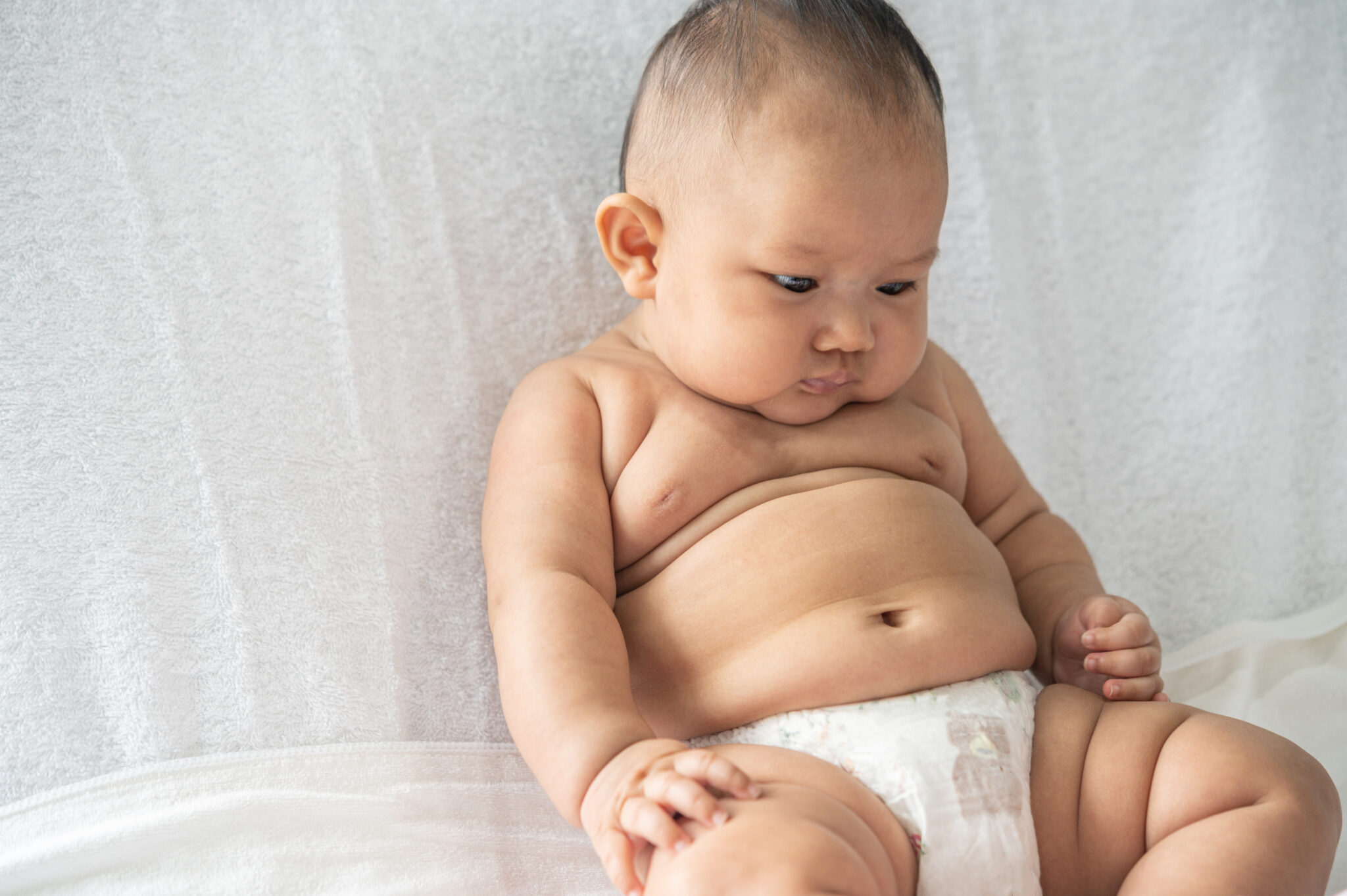 A baby learns to sit on a white bed