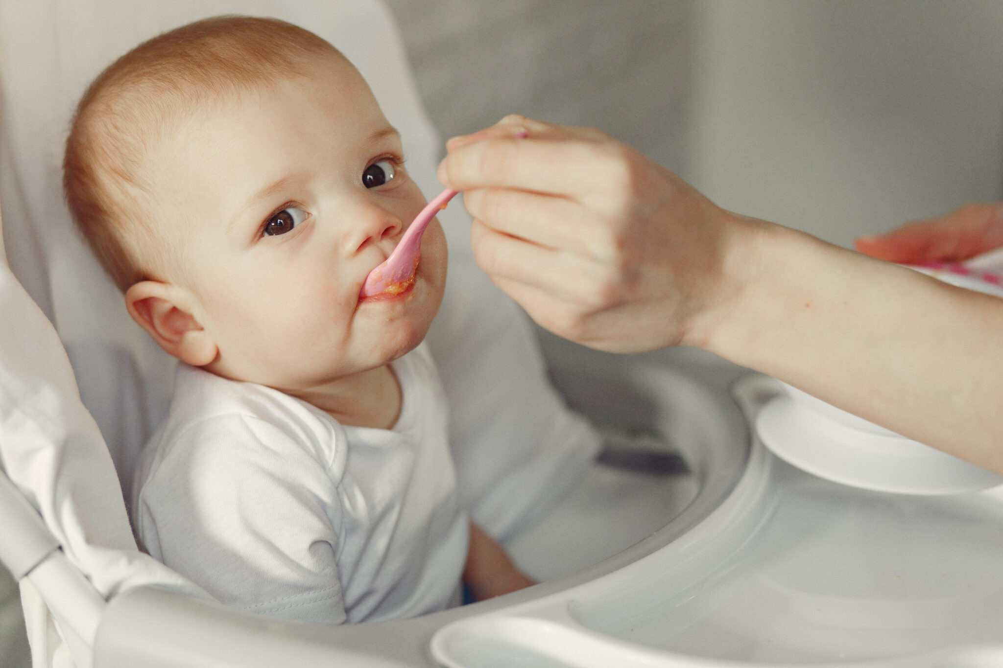 Baby eating. Mother feeds the baby. Little child in a kid's chair.